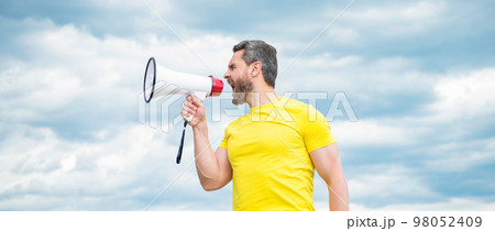 man in yellow shirt yelling in loudspeaker on sky background 98052409