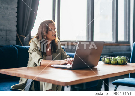 Woman at home sits at her desk and looks at her laptop screen 98053151