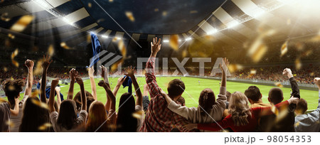 Back view of football, soccer fans cheering their team, holding flag at crowded stadium at evening time. Concept of sport, hobby, leisure time, football Back view of football, soccer fans cheering their team, holding flag at crowded stadium at evening time. Concept of sport, hobby, leisure time, football 98054353