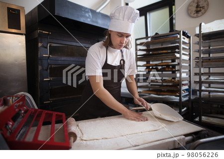 Young baker with chef cap preparing pastries in bakery. Young baker with chef cap preparing pastries in bakery. 98056226