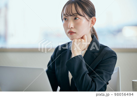 デスクで頬杖をついて考え事をする若い女性 98056494