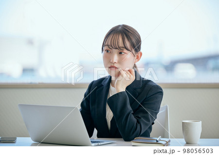 デスクで頬杖をついて考え事をする若い女性 98056503