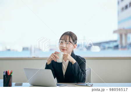 デスクでコーヒーを飲みながら休憩をする若い女性 98056517