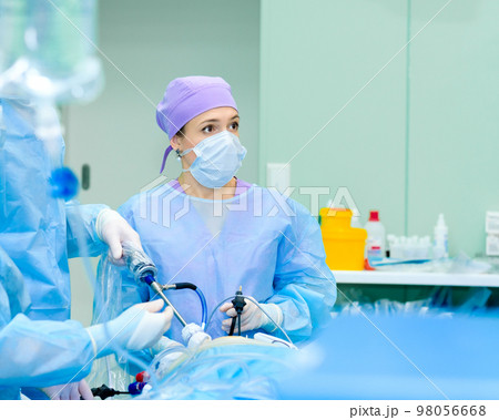 Focused female surgeon performs laparoscopic surgery in the operating room. 98056668