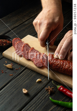 Cutting sausage on wooden cutting board at domestic kitchen by hands chef for a sandwich. 98057238