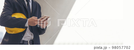 Banner Construction engineer holding yellow hard hat holding smartphone. Panorama Safety helmet Holding Yellow hardhat using phone Construction Site. Banner Hardhat Civil Construction with copy space 98057702