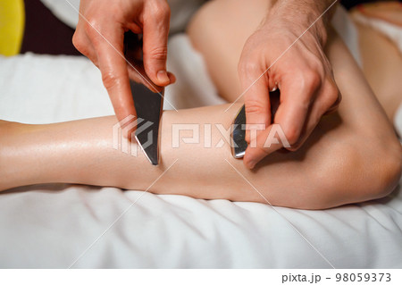 Masseur using IASTM instrument for soft tissue treatment on the leg of a female patient 98059373