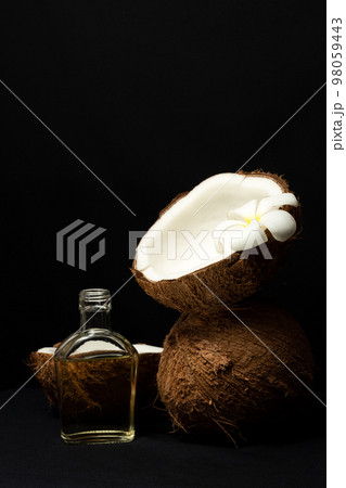 Tropical fruit concept, Halves of fresh coconut and bottle of coconut oil on black background Tropical fruit concept, Halves of fresh coconut and bottle of coconut oil on black background 98059443