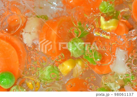 Close-up fresh soup vegetables with carrots, peas, cauliflower and corn on white background. Soup vegetables with carrots, peas, cauliflower and corn in boiling water on white background, close-up. 98061137