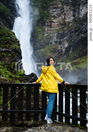 Girl tourist in yellow jacket enjoys freedom against backdrop of waterfall. Travelling, lifestyle. 98061213