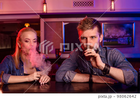 A man and woman smoking electronic cigarette in a vape bar. 98062642
