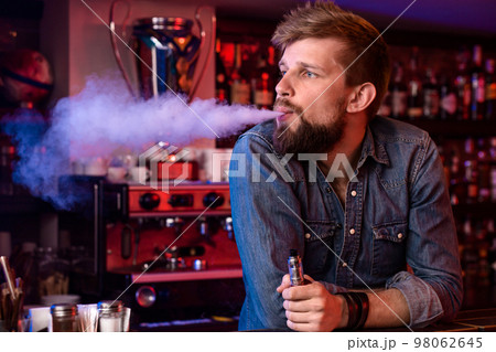 Vape. Vaping man in a cloud of vapor. Photo is taken in a vape bar. Vape. Vaping man in a cloud of vapor. Photo is taken in a vape bar. 98062645