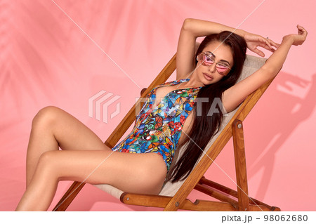Woman relaxing on beach chair. Sun bath with hat, sunglasses and various expressions, studio shot 98062680
