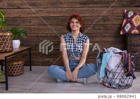 A smiling girl in a plaid shirt sits on the floor next to the laundry. A smiling girl in a plaid shirt sits on the floor next to the laundry. 98062941