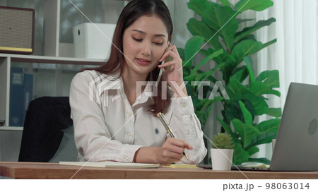 Young enthusiastic businesswoman talking on business call and taking note. 98063014