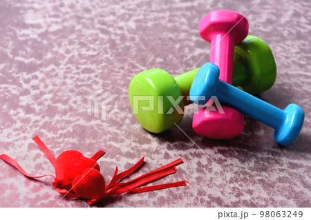 Dumbbells made of pink, green and cyan plastic near hearts Dumbbells made of pink, green and cyan plastic near hearts 98063249