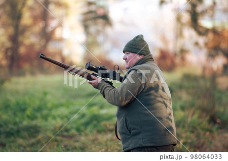 Autumn hunting season, hunter with rifle looking out for some wild animal in a wood or forest, outdoor sports concept 98064033