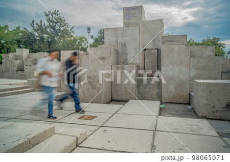 two people walking, long exposure blur, in the background stone sculpture different levels 98065071