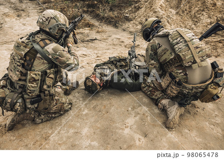 Wounded man lying on a ground, other soldiesr next to him 98065478