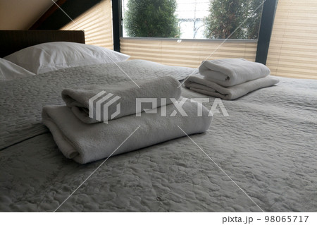 There are clean white towels on the bed. Hotel room. 98065717
