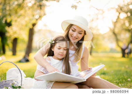 A mother and daughter in the spring garden on a plaid leaf through and look through a book with photos from a family photo shoot. Remember the important moments of life in the photo album. 98066094