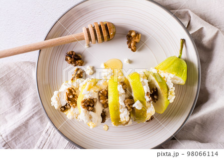 Pear with ricotta, honey and walnuts in layers on a plate. Healthy food. Top view. Closeup Pear with ricotta, honey and walnuts in layers on a plate. Healthy food. Top view. Closeup 98066114