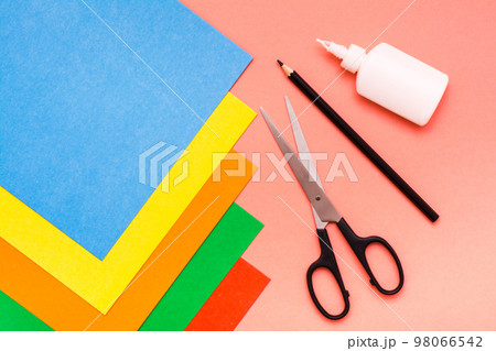 Items for creativity - sheets of colored cardboard, scissors, pencil and glue on a red background. Top View 98066542