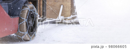 Tractor wheel with chain. Tractor or loader on a slippery snowy road. Loaders drive on snow with anti-skid chains. Tractor wheel with chain. Tractor or loader on a slippery snowy road. Loaders drive on snow with anti-skid chains. 98066605