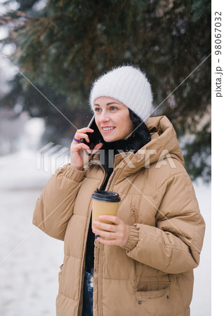 Cute girl talking on the phone and drinking coffee outside in winter 98067032