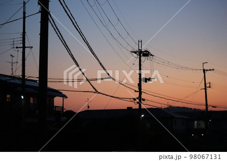 青空と朝焼けの茜色の空と黒いシルエットの町並みと電線と電柱の見える早朝の風景 98067131