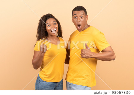 Joyful young african american couple celebrating success with thumb up and clenched fists, yellow background 98067330
