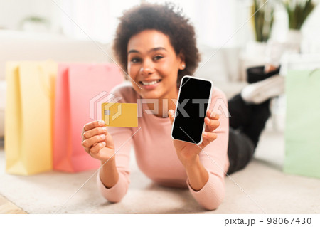 App for online shopping at home. Glad young mixed race lady shopaholic shows phone and credit card 98067430