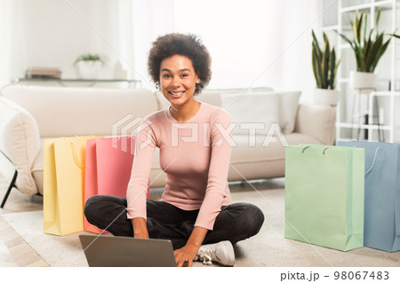 Shopaholic, fashion blogger. Smiling young mixed race female typing on laptop on floor in living room Shopaholic, fashion blogger. Smiling young mixed race female typing on laptop on floor in living room 98067483