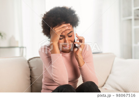 Despaired sad depressed young mixed race lady sitting on sofa, calling by smartphone, presses hand to head Despaired sad depressed young mixed race lady sitting on sofa, calling by smartphone, presses hand to head 98067516