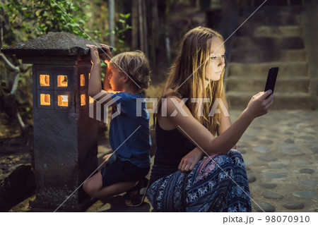 Mom looks into her smartphone, the son looks into the luminous cozy window of the house. The boy lacks Attention, care, love and home comfort Mom looks into her smartphone, the son looks into the luminous cozy window of the house. The boy lacks Attention, care, love and home comfort 98070910