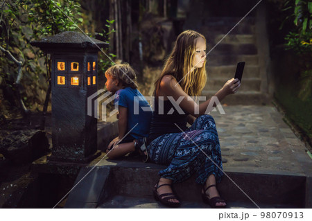 Mom looks into her smartphone, the son looks into the luminous cozy window of the house. The boy lacks Attention, care, love and home comfort Mom looks into her smartphone, the son looks into the luminous cozy window of the house. The boy lacks Attention, care, love and home comfort 98070913