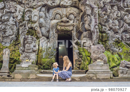 Mom and son are tourists in Old Hindu temple of Goa Gajah near Ubud on the island of Bali, Indonesia. Travel in Bali with children concept Mom and son are tourists in Old Hindu temple of Goa Gajah near Ubud on the island of Bali, Indonesia. Travel in Bali with children concept 98070927