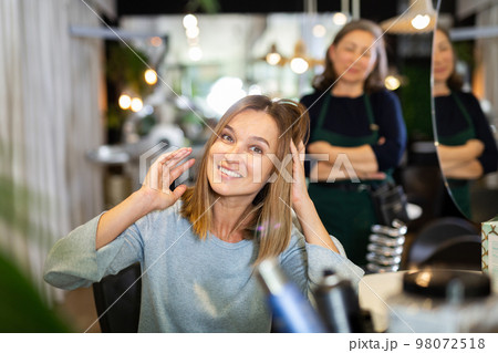 Young woman looking satisfied with hairdo in hairdressing salon 98072518
