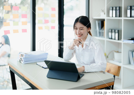 Portrait of a thoughtful Asian businesswoman looking at financial statements and making marketing plans using a computer on her desk. Portrait of a thoughtful Asian businesswoman looking at financial statements and making marketing plans using a computer on her desk. 98082005