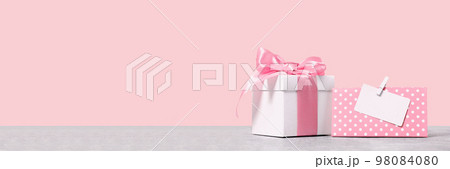 White gift box with shining pink ribbon bow on pink background with mockup gift card. Gift or holiday concept. Mothers Day, birthday wedding or St Valentines day banner with copy space 98084080