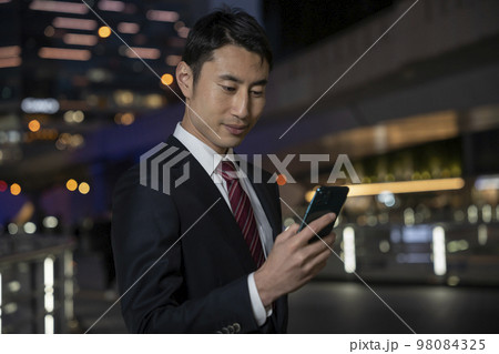 スマートフォンの画面を見るビジネスマン　夜のビル街 98084325