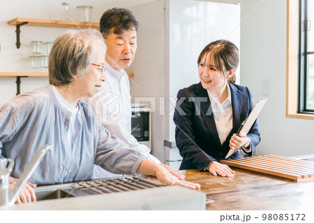住宅展示場・モデルルーム・ハウスメーカーで高齢者夫婦に説明するビジネスウーマン（キッチン・天板） 98085172