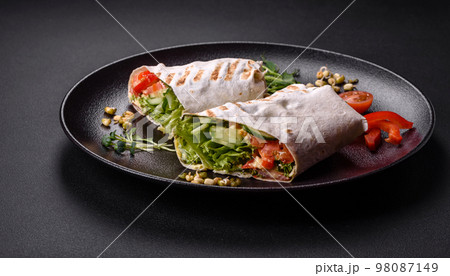 Delicious fresh shawarma with tomatoes, peppers, cucumber on a dark concrete background Delicious fresh shawarma with tomatoes, peppers, cucumber on a dark concrete background 98087149