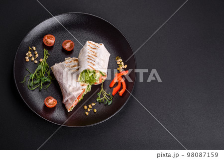 Delicious fresh shawarma with tomatoes, peppers, cucumber on a dark concrete background 98087159