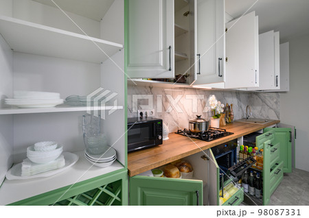 Doors open and drawers pulled out at new green and white kitchen furniture 98087331