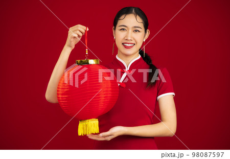 Smiling young asian woman in red traditional chinese dress holding red paper lantern on red background. Chinese New Year concept.	 98087597