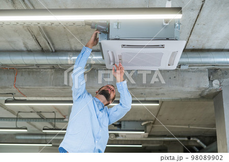Caucasian bearded man repairing the air conditioner in the office.  Caucasian bearded man repairing the air conditioner in the office.  98089902