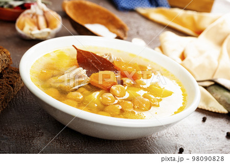 Hot spicy soup with chickpeas, onions in ceramic bowl on a dark background close-up. 98090828