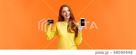 Shopping, online and finance concept. Cheerful young redhead female opened bank account, holding smartphone and credit card, smiling, recommend use online shopping application Shopping, online and finance concept. Cheerful young redhead female opened bank account, holding smartphone and credit card, smiling, recommend use online shopping application 98090998