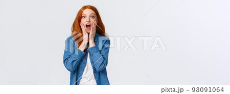Oh my gosh, amazing. Surprised speechless redhead woman standing starled and shocked, touch face, drop jaw and stare camera fascinated, got job, won prize, standing white background 98091064
